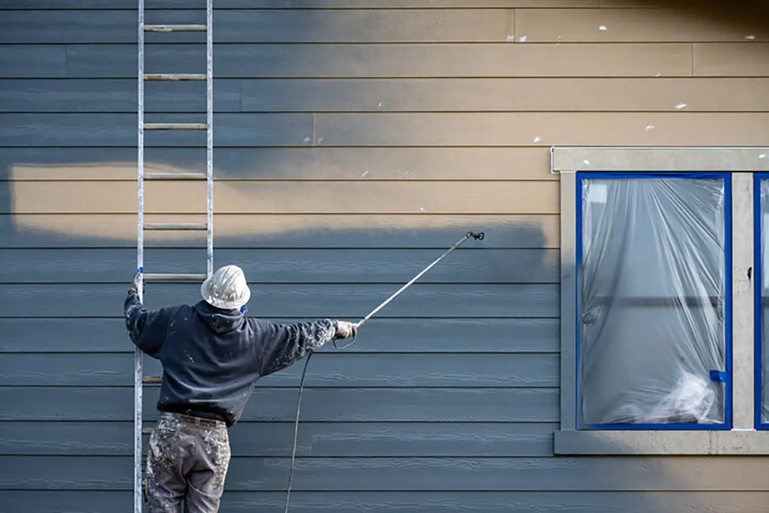 Professional painter spray painting exterior house siding with two-tone color application