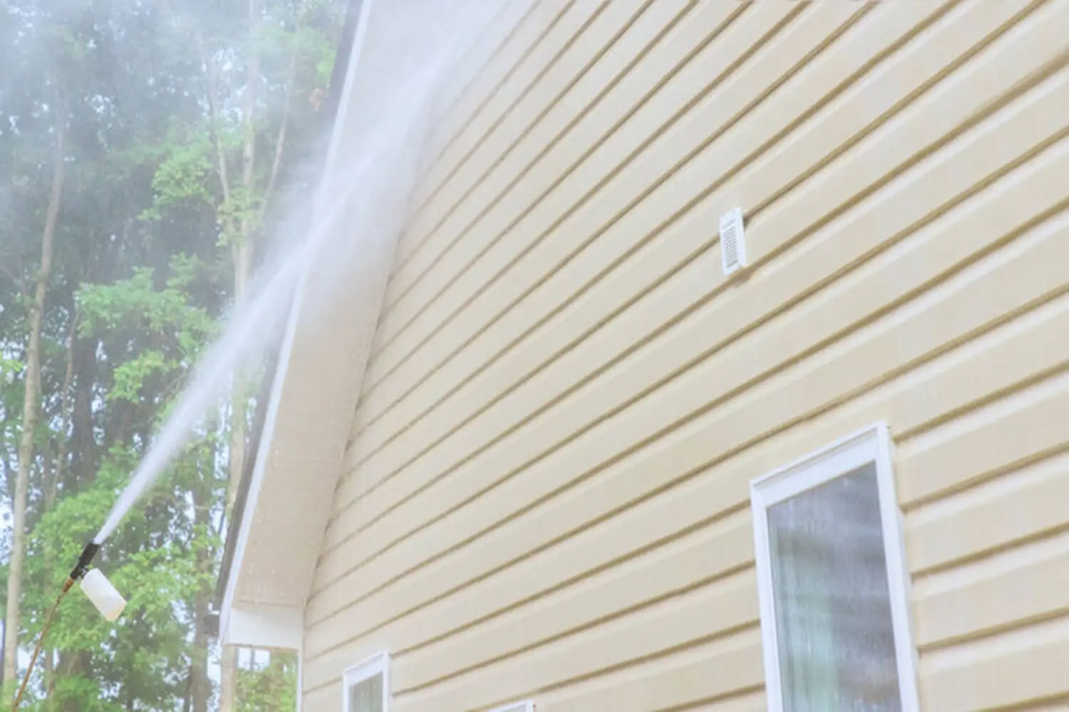 Pressure washer spraying water across the exterior siding of a residential home showing signs it needs pressure washing.